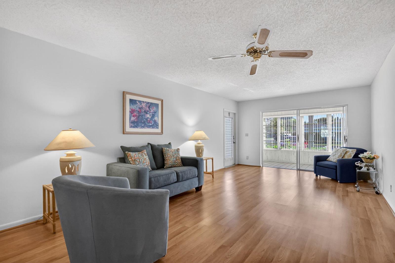 A living room features light wood flooring, a ceiling fan, a sofa, and sliding glass doors — 5091 Lakefront Boulevard # C, Delray Beach FL 33484, DELRAY BEACH, FL