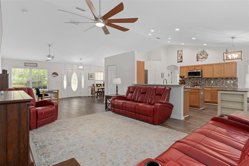 An open-concept living room with red leather furniture, wood-look flooring, and an adjacent kitchen — 7 BIGLEAF COURT, HOMOSASSA, FL