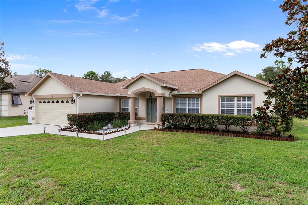 A single-story house with a tan stucco exterior, a brown shingled roof, and a front lawn — 7 BIGLEAF COURT, HOMOSASSA, FL
