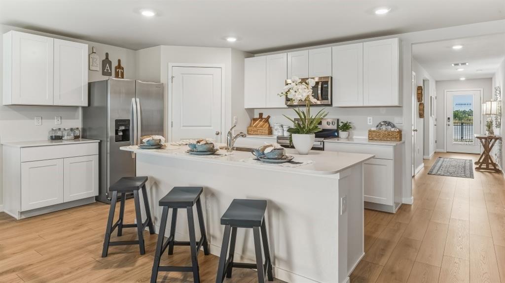 A white kitchen features a central island with three stools and light wood flooring — 9620 TURTLE GRASS CIRCLE, PUNTA GORDA, FL