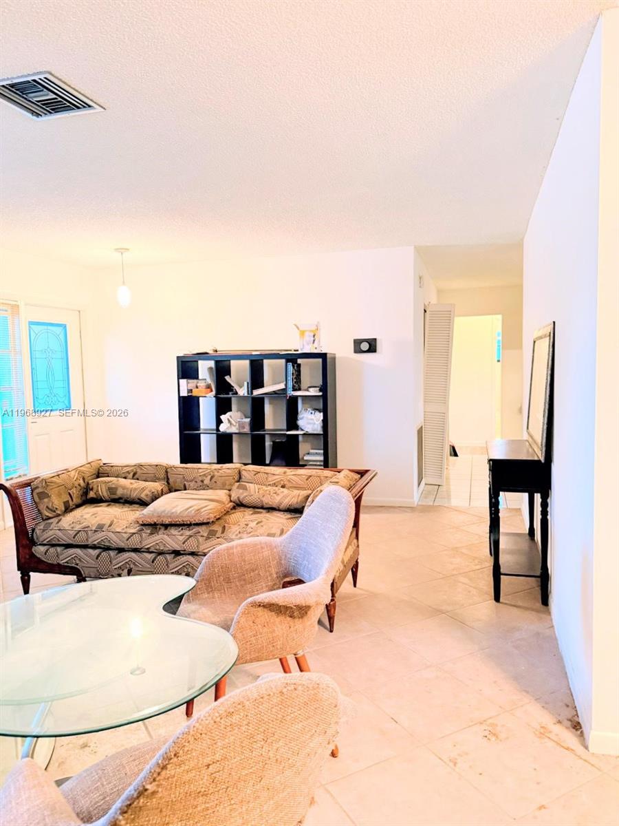 A living room features tile flooring, a patterned sofa, a black shelving unit, and furniture — 766 NW 24th Ave, Delray Beach FL 33445, DELRAY BEACH, FL