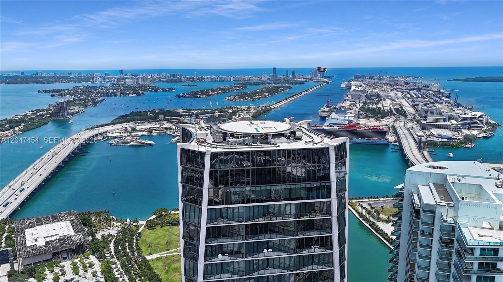 An aerial view shows a modern glass skyscraper with a rooftop helipad near a harbor — 1000 Biscayne Blvd # 4401, Miami FL 33132, MIAMI, FL