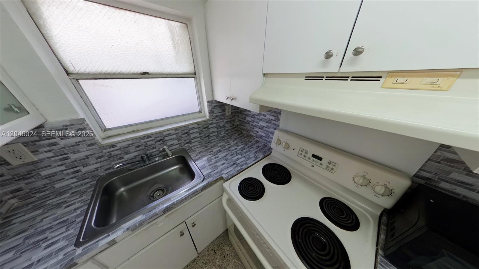 A small kitchen features a stainless steel sink, electric stove, and gray tiled backsplash — 2712 W 10th Ave # 5, Hialeah FL 33010, HIALEAH, FL