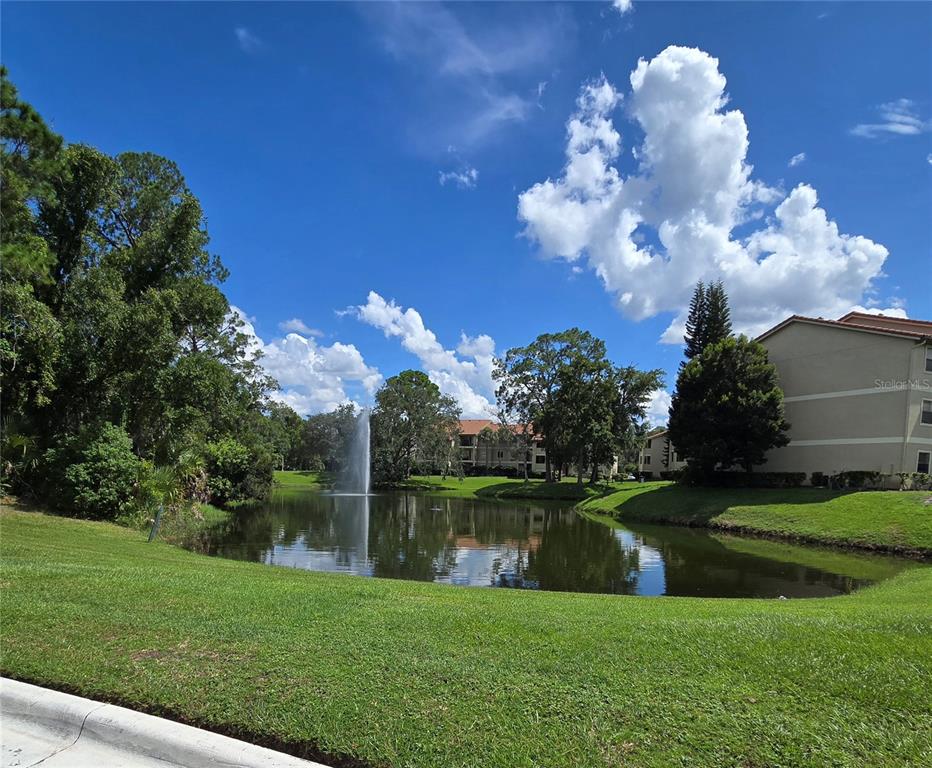 A pond with a fountain is surrounded by green grass, trees, and apartment buildings — 3100 PARKWAY BOULEVARD UNIT 752, KISSIMMEE, FL