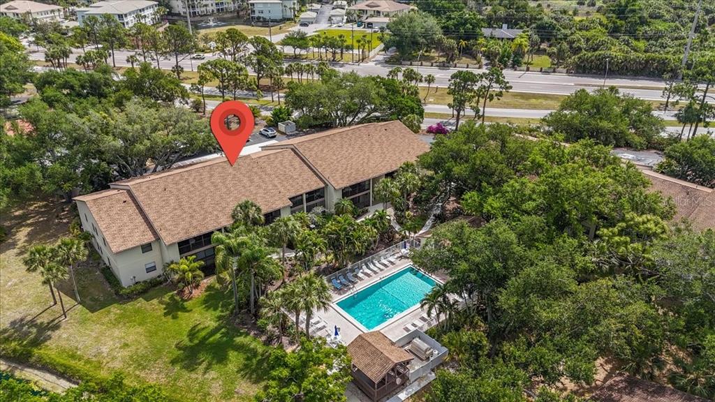 An aerial view shows a multi-story apartment building with a swimming pool and surrounding trees — 646 BIRD BAY DRIVE E UNIT 205, VENICE, FL