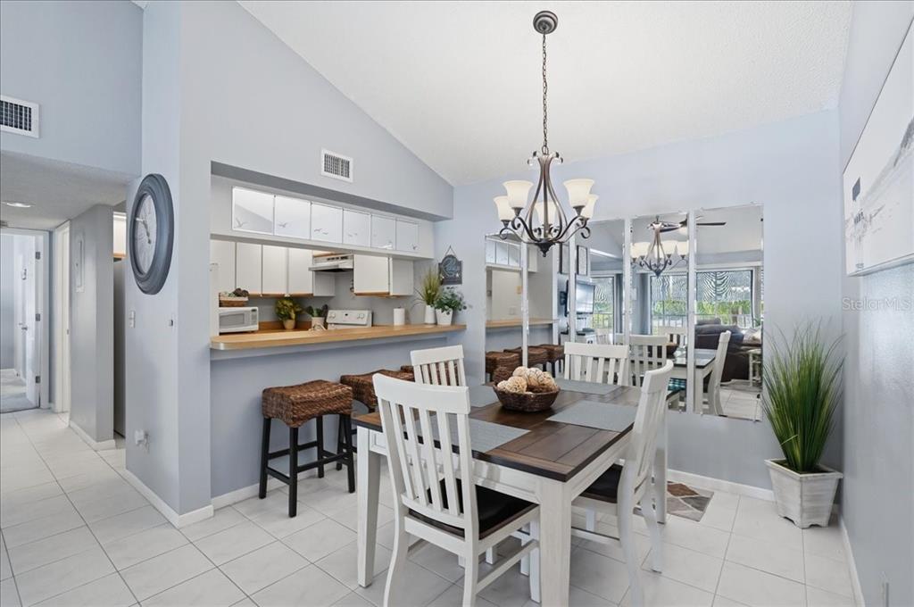 A dining area features a wooden table, white chairs, a breakfast bar, and mirrored walls — 646 BIRD BAY DRIVE E UNIT 205, VENICE, FL