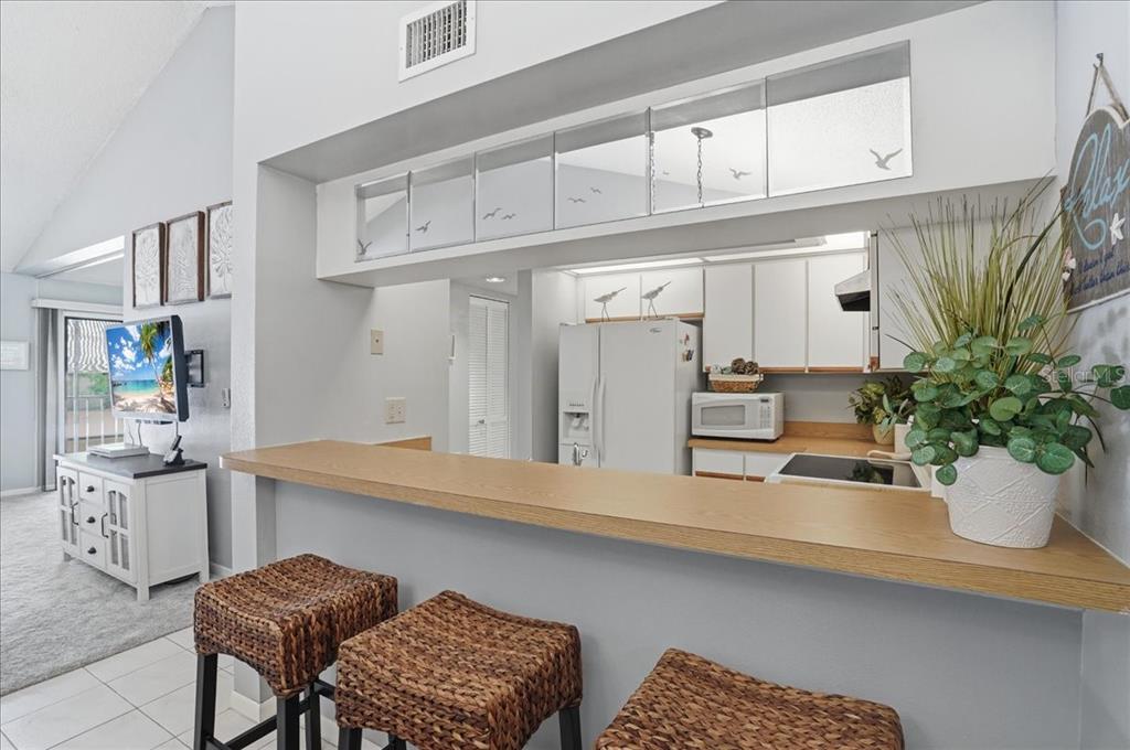 A kitchen with white cabinets and a breakfast bar overlooking a living area — 646 BIRD BAY DRIVE E UNIT 205, VENICE, FL