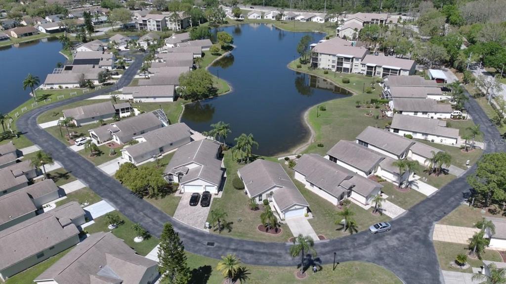 An aerial view shows a residential community with houses surrounding a central lake — 4429 WHITTON WAY, NEW PORT RICHEY, FL
