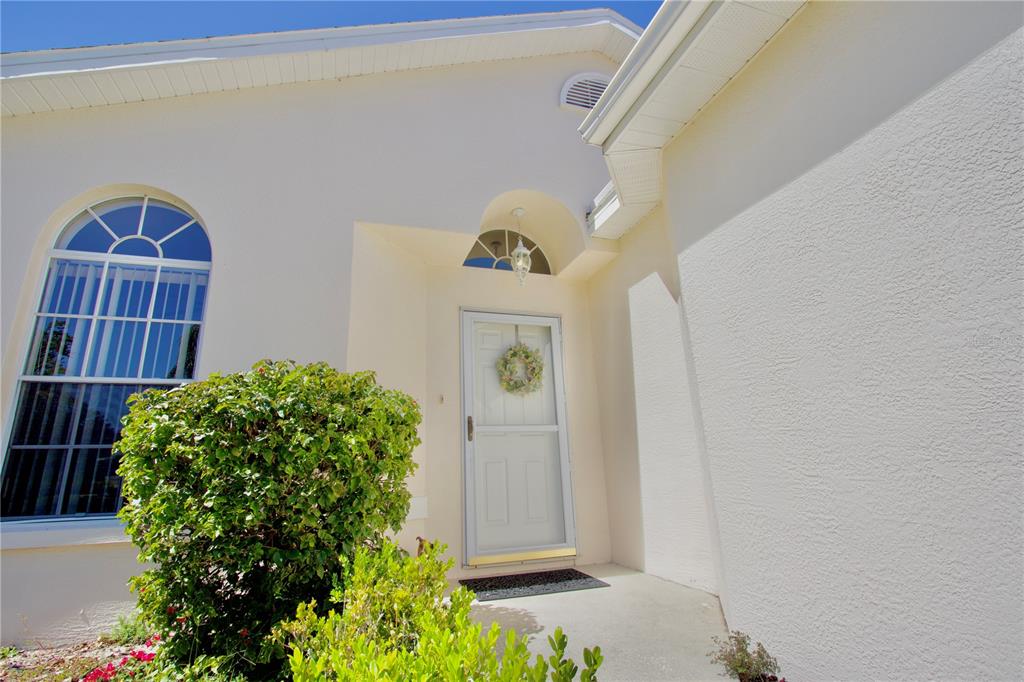 A white house exterior features a front door with a storm door and a large window — 4429 WHITTON WAY, NEW PORT RICHEY, FL
