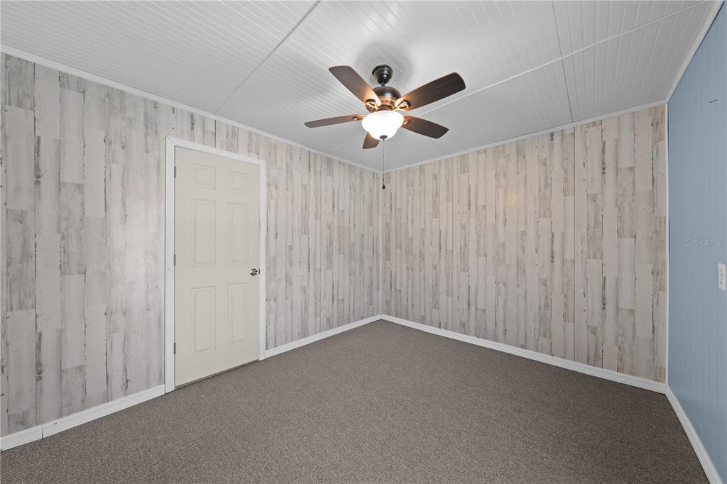 An empty room features wood-look wallpaper, gray carpeting, a white ceiling, and a ceiling fan — 683 JOHN HANCOCK LANE, WEST MELBOURNE, FL