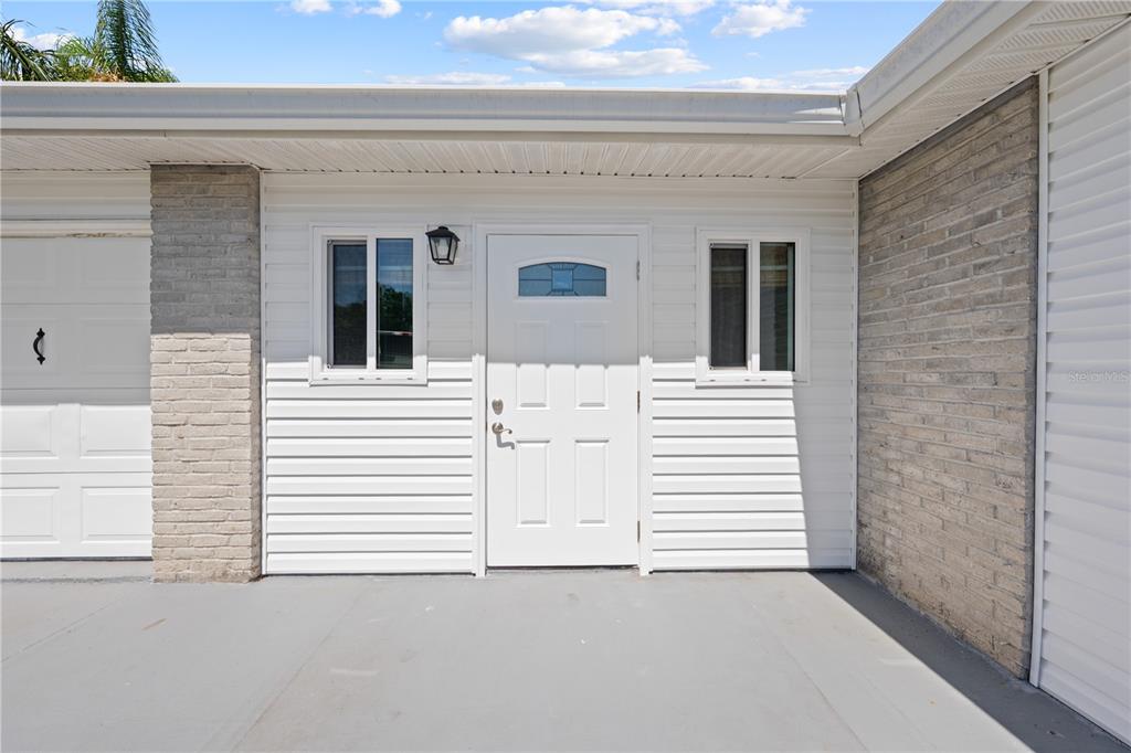 A white front door is centered between two windows on a house exterior with siding — 683 JOHN HANCOCK LANE, WEST MELBOURNE, FL