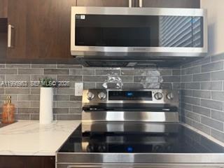 A stainless steel microwave and electric range are set against a gray tiled backsplash — 1607 NW 16th Ave # 1, Miami FL 33125, MIAMI, FL