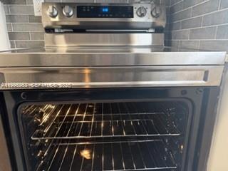 A stainless steel electric range with a glass cooktop is set against a tiled backsplash — 1607 NW 16th Ave # 1, Miami FL 33125, MIAMI, FL