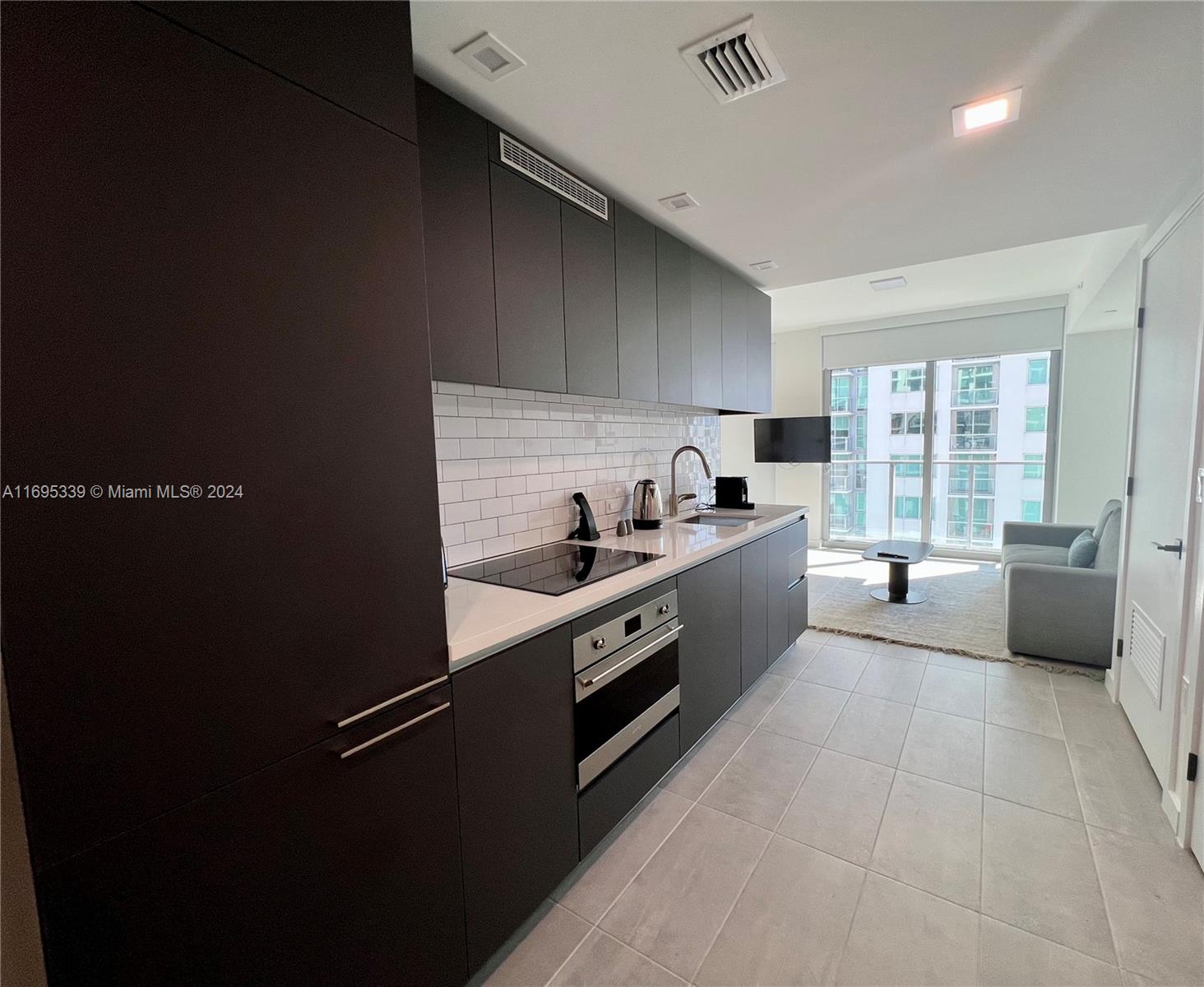 A modern kitchen with dark cabinetry, white subway tile, and stainless steel appliances — 227 NE 2nd St # 2613, Miami FL 33132, MIAMI, FL