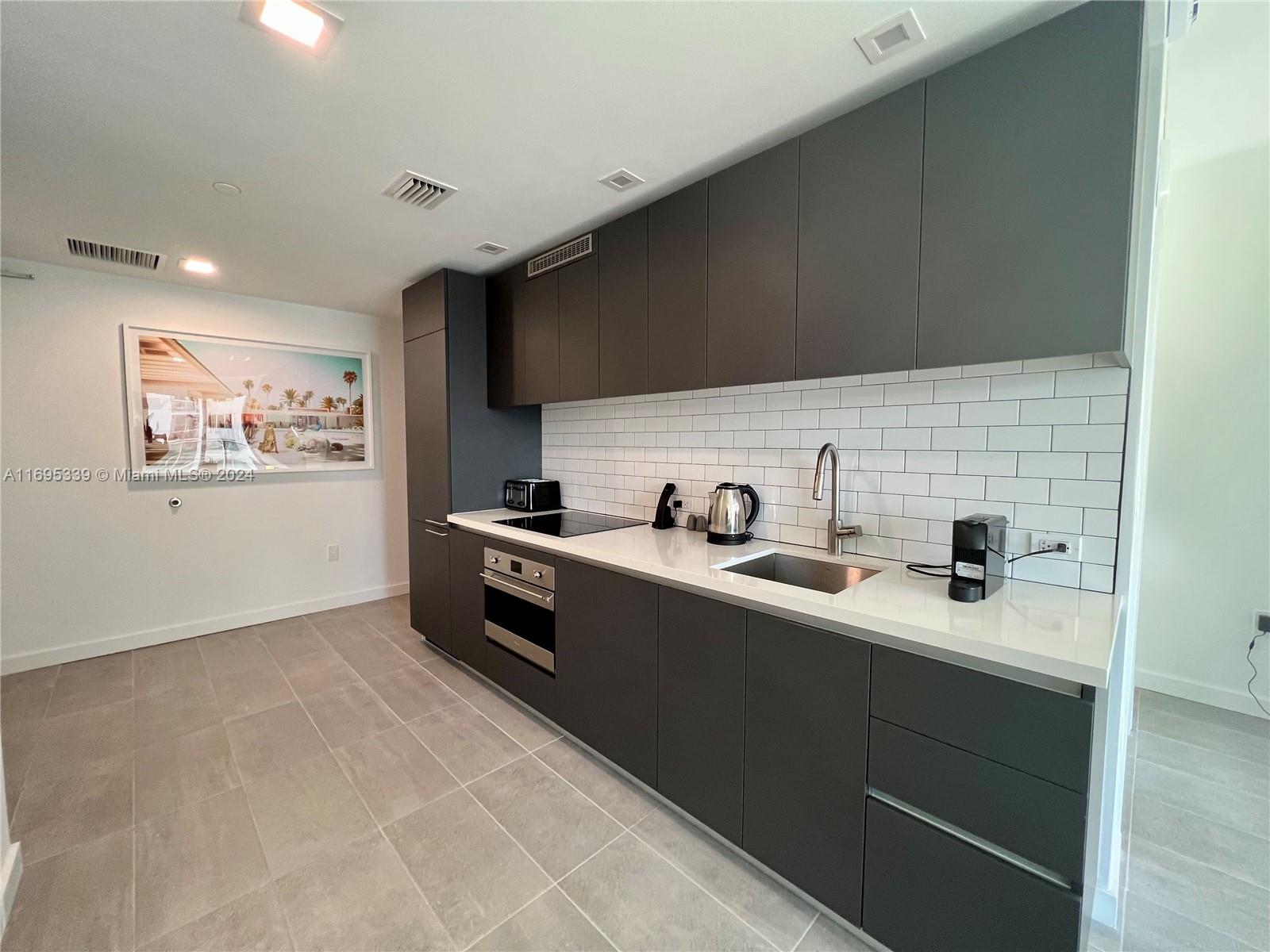 A modern kitchen features dark gray flat-panel cabinets, white countertops, and a white subway tile backsplash — 227 NE 2nd St # 2613, Miami FL 33132, MIAMI, FL