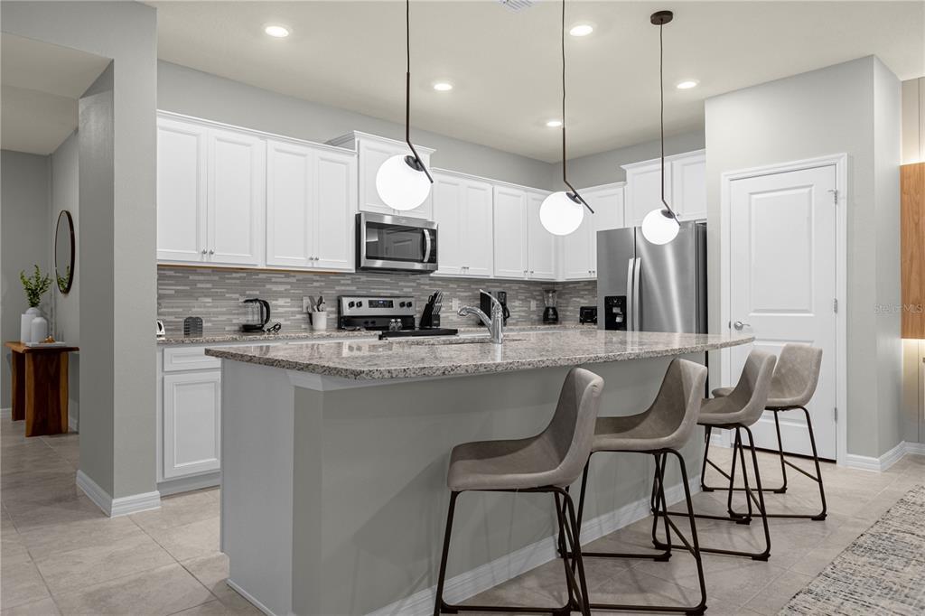 A modern kitchen features white cabinetry, granite countertops, a central island, and three pendant lights — 4358 LANA AVENUE, DAVENPORT, FL