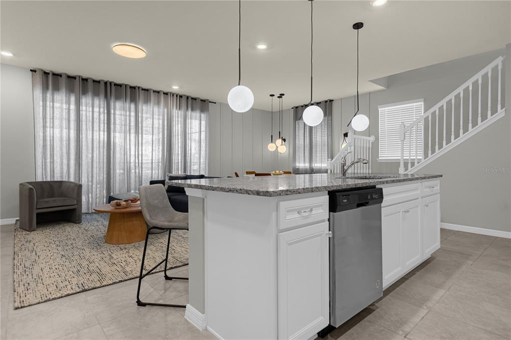 A kitchen island with a granite countertop and dishwasher faces a living area with curtains — 4358 LANA AVENUE, DAVENPORT, FL
