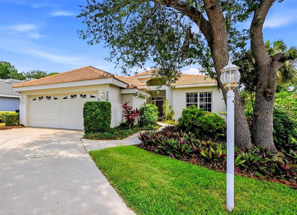 A single-story house with a white garage, tile roof, and a front yard with trees — 238 VESTAVIA DRIVE, VENICE, FL
