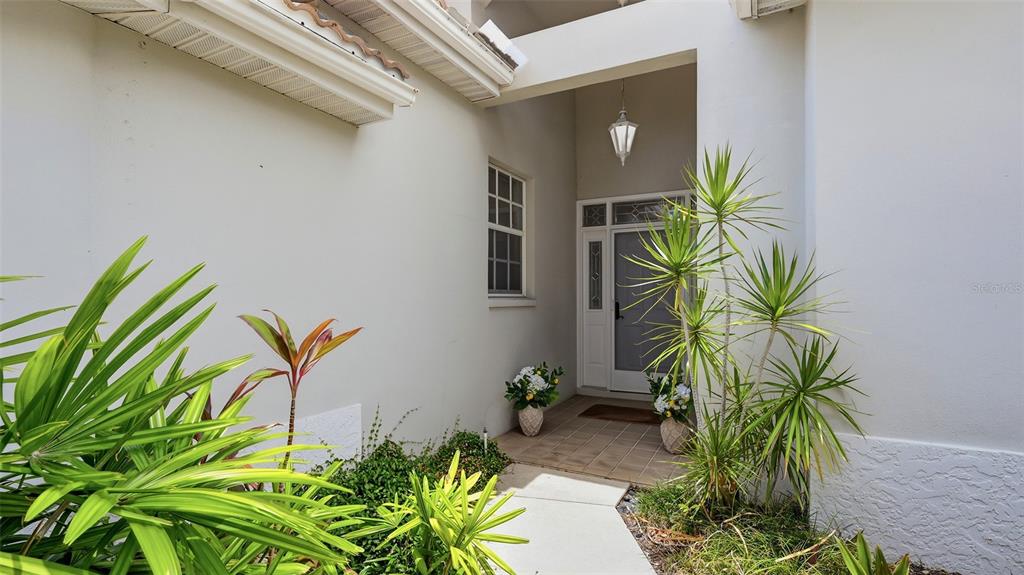 A concrete walkway leads to the covered front entrance of a house with light-colored walls — 238 VESTAVIA DRIVE, VENICE, FL