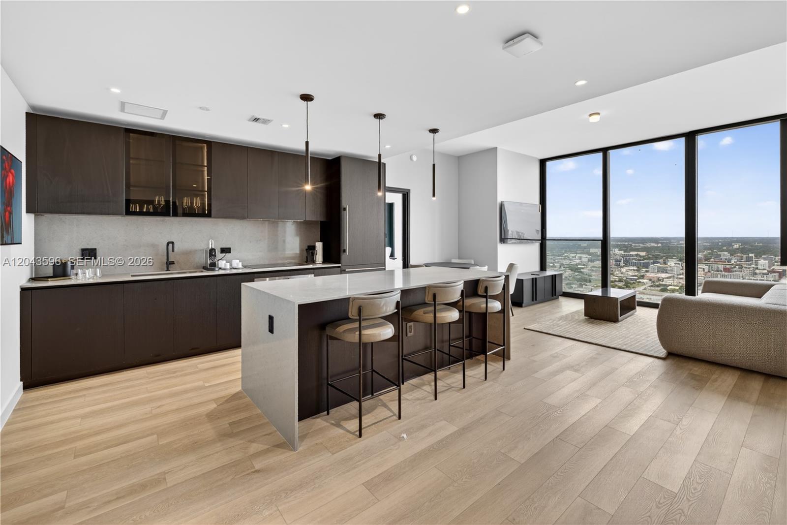 A modern kitchen features dark wood cabinetry, a white stone island, and floor-to-ceiling windows — 20 NE 11th # 4702, Miami FL 33132, MIAMI, FL