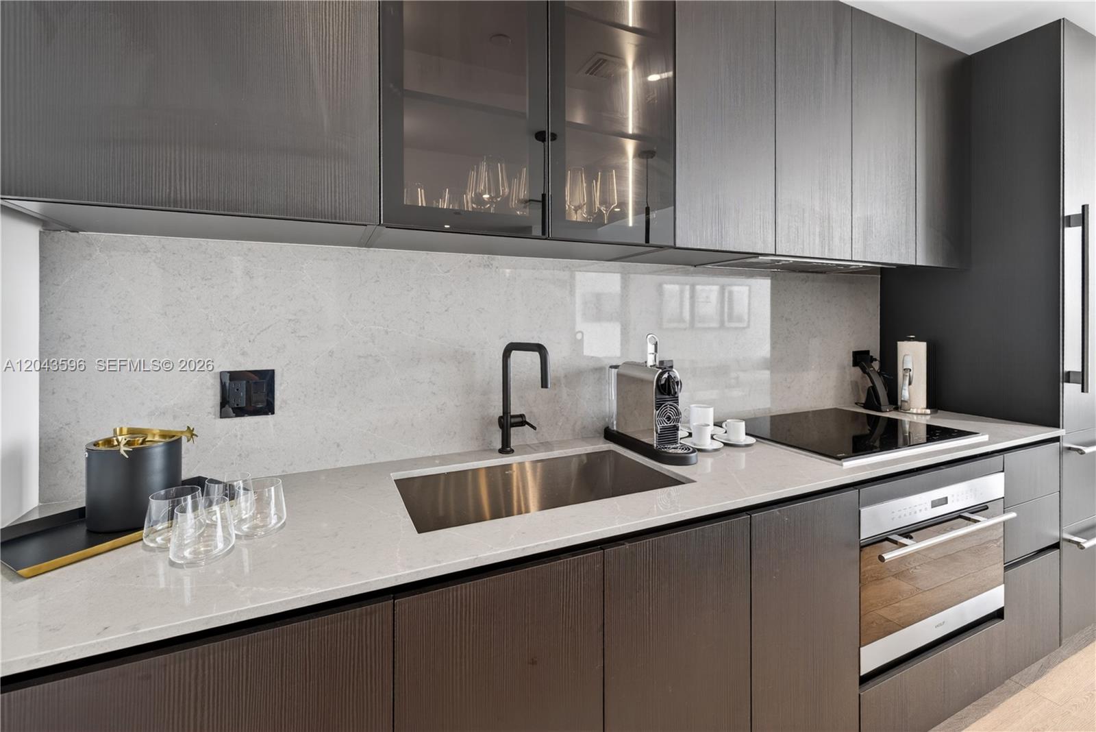 A modern kitchen features dark wood cabinetry, a light stone countertop, and a stainless sink — 20 NE 11th # 4702, Miami FL 33132, MIAMI, FL