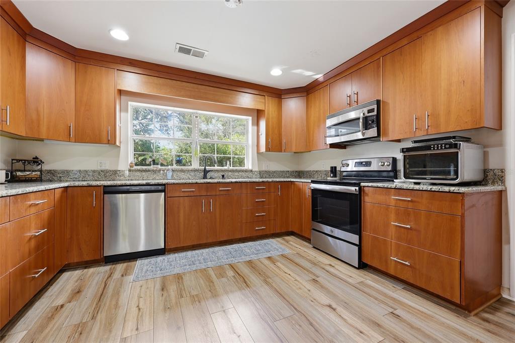 A kitchen features wood cabinets, stainless steel appliances, granite countertops, and light wood-look flooring — 812 NW 36TH TERRACE, GAINESVILLE, FL