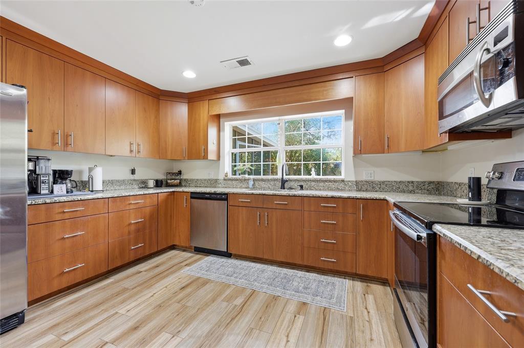 A kitchen features wood cabinets, granite countertops, stainless steel appliances, and light wood-look flooring — 812 NW 36TH TERRACE, GAINESVILLE, FL