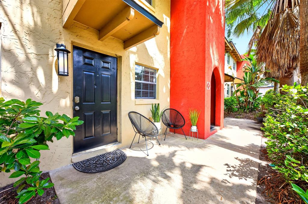 A black front door sits on a concrete patio beside two chairs and red walls — 2423 E CENTRAL BOULEVARD UNIT 1, ORLANDO, FL