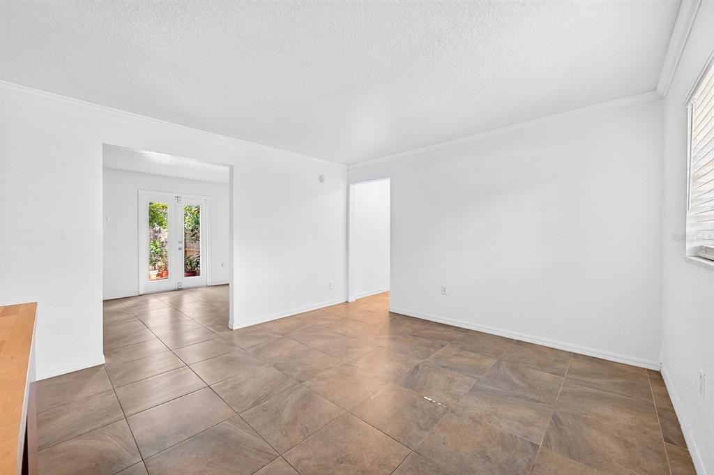 A bright, empty room features white walls, crown molding, and large, square brown floor tiles — 2423 E CENTRAL BOULEVARD UNIT 1, ORLANDO, FL
