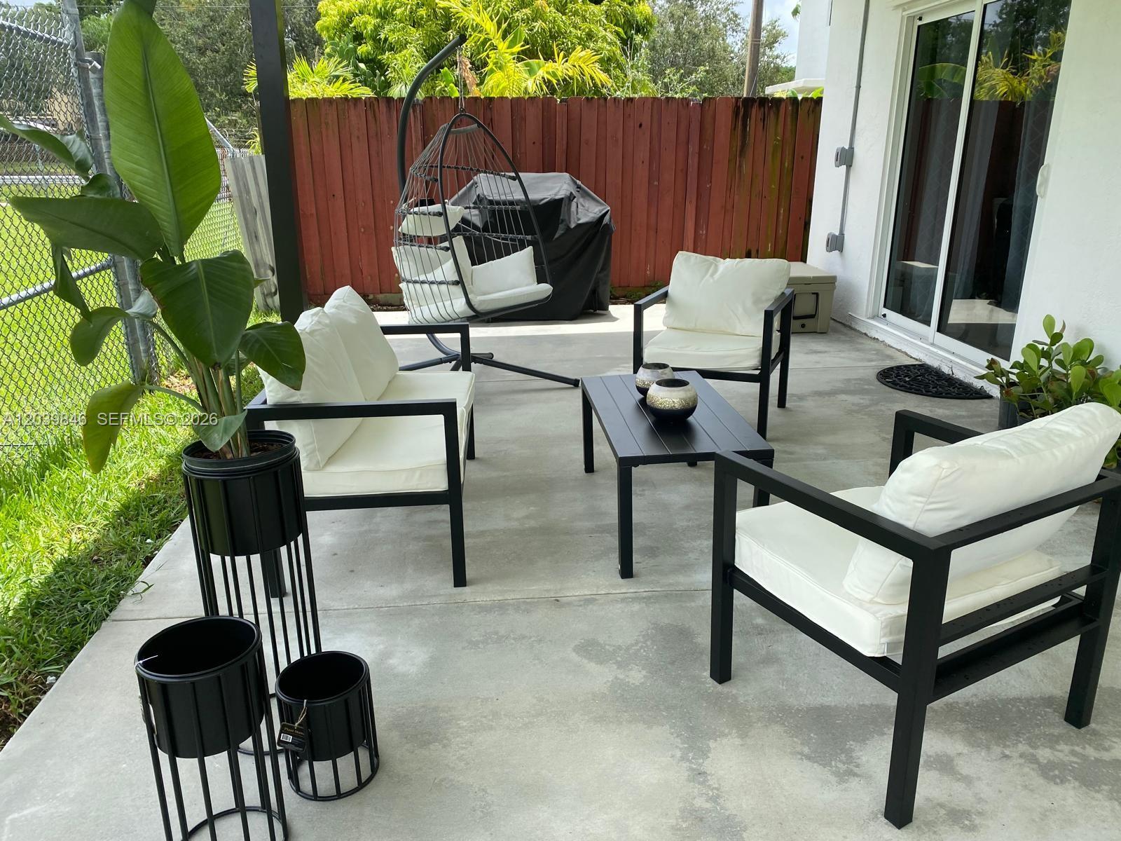 A patio features black metal outdoor furniture, white cushions, a hanging chair, and potted plants — 8121 SW 136th Pl # 8121, Miami FL 33183, MIAMI, FL
