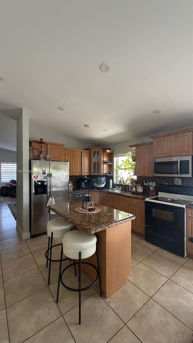 A kitchen features wood cabinets, granite countertops, a center island with stools, and tile flooring — 8121 SW 136th Pl # 8121, Miami FL 33183, MIAMI, FL