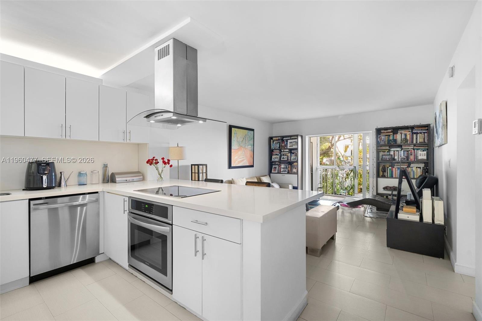 A modern white kitchen with stainless steel appliances opens into a living area with bookshelves — 240 Galen Drive # 109, Key Biscayne FL 33149, KEY BISCAYNE, FL
