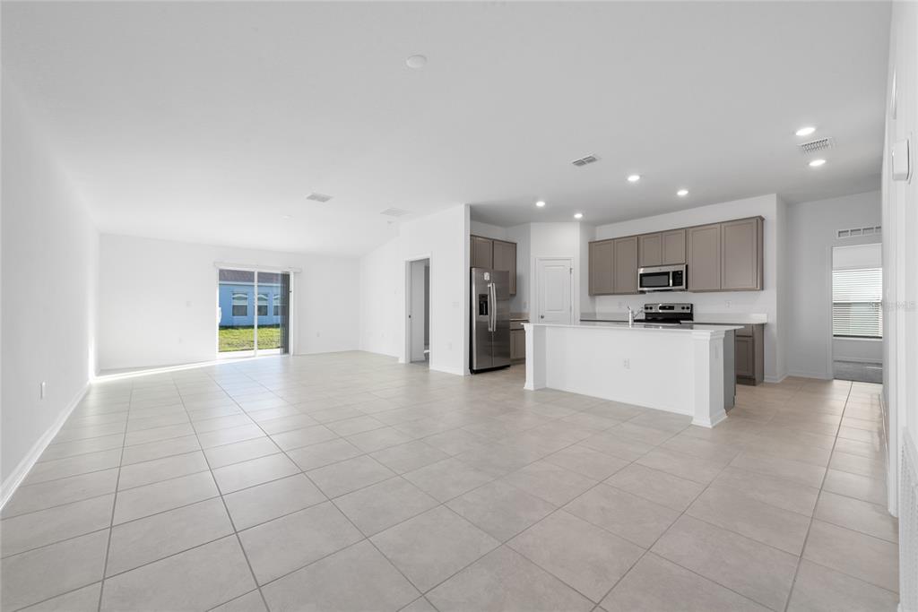 An open-concept living area features light tile flooring, a kitchen with gray cabinets, and appliances — 338 RUSTIC RAIL DRIVE, LAKE WALES, FL