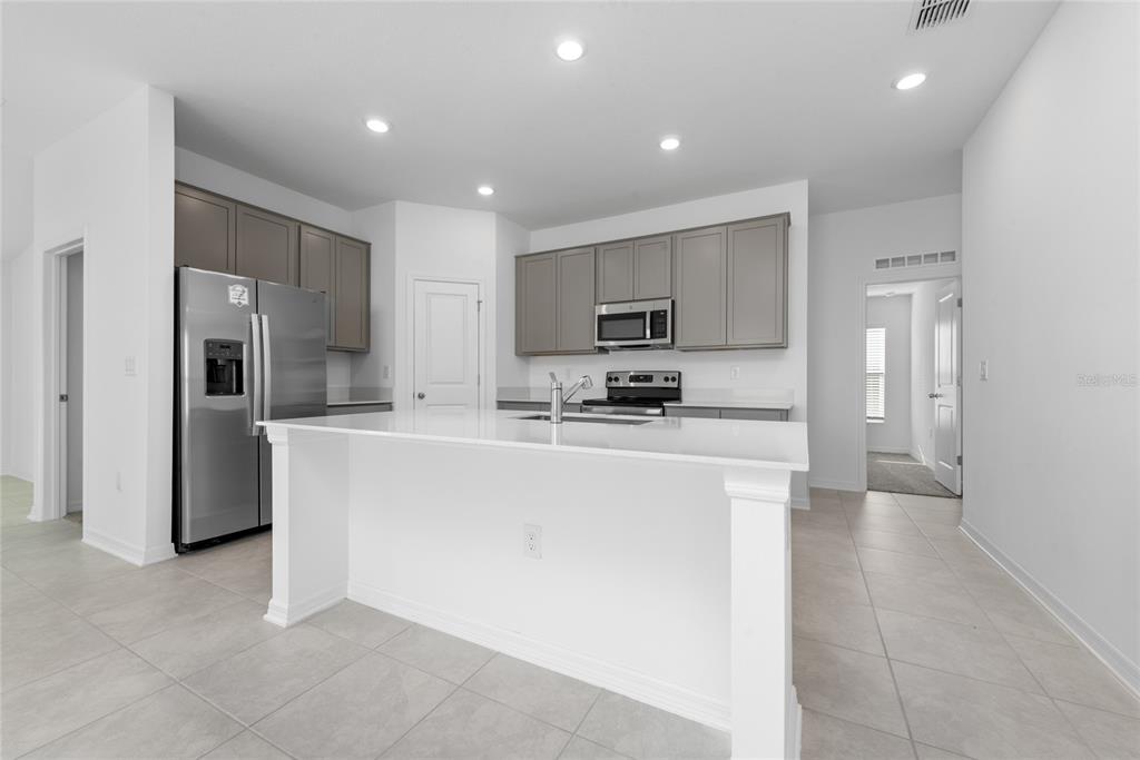 A modern kitchen features gray cabinets, stainless steel appliances, and a white quartz island — 338 RUSTIC RAIL DRIVE, LAKE WALES, FL