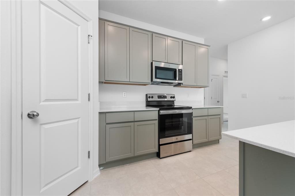 A kitchen features gray cabinets, stainless steel appliances, white countertops, and light tile flooring — 338 RUSTIC RAIL DRIVE, LAKE WALES, FL