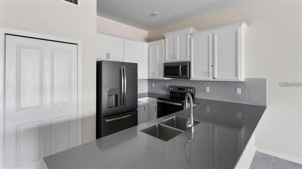 A kitchen features white cabinets, gray countertops, a stainless steel refrigerator, and a sink island — 857 OCEAN COURSE AVENUE UNIT 857, DAVENPORT, FL