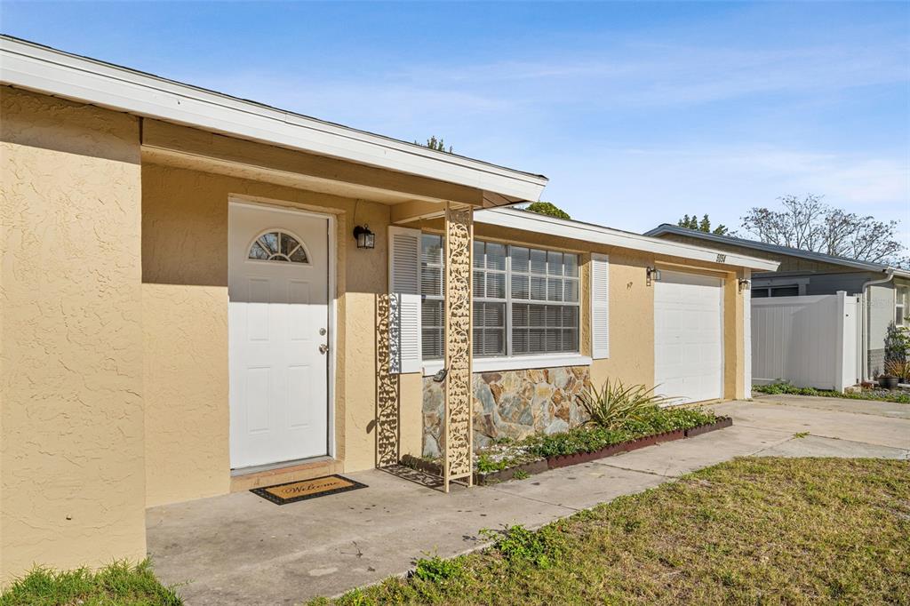 A single-story house with a tan stucco exterior, a white front door, and a garage — 5054 SCHOOL ROAD, NEW PORT RICHEY, FL