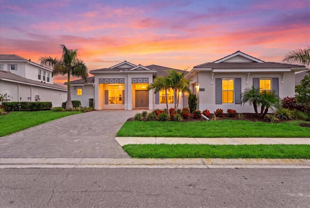 A single-story house with a paved driveway, palm trees, and a sunset sky — 8133 NEVIS RUN, BRADENTON, FL