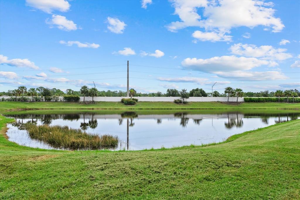 A grassy lawn slopes down toward a retention pond with a white fence in back — 8133 NEVIS RUN, BRADENTON, FL