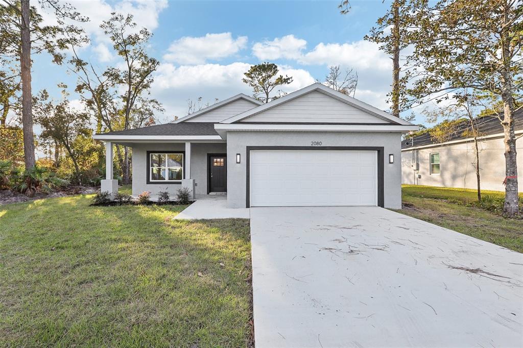 A single-story house with a gray stucco exterior, a white garage door, and a front porch — 1885 9TH AVENUE, DELAND, FL