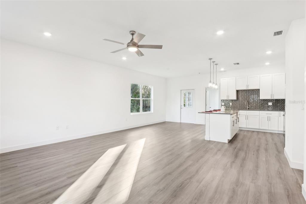 An open-concept living room and kitchen with white cabinets, a center island, and wood flooring — 1885 9TH AVENUE, DELAND, FL