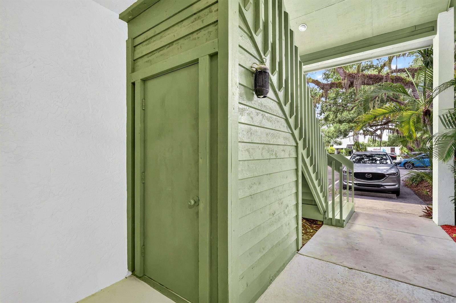 A green storage closet is located beneath an outdoor wooden staircase on a concrete walkway — 5250 SE Seascape Way # 102, Stuart FL 34997, STUART, FL