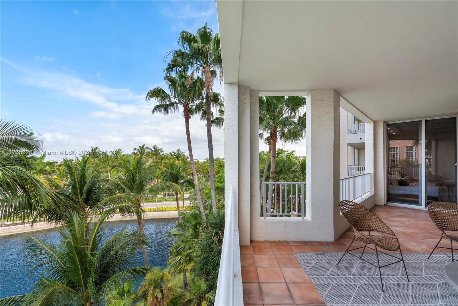A tiled balcony overlooks a canal and palm trees with two wicker chairs — 705 Crandon Blvd # 405, Key Biscayne FL 33149, KEY BISCAYNE, FL