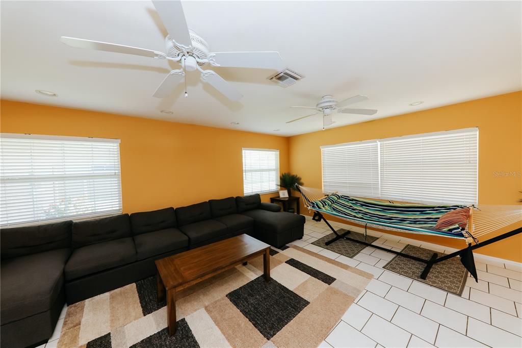 A living room features orange walls, a large sectional sofa, and a hammock on tiles — 5211 24TH AVENUE DRIVE W, BRADENTON, FL