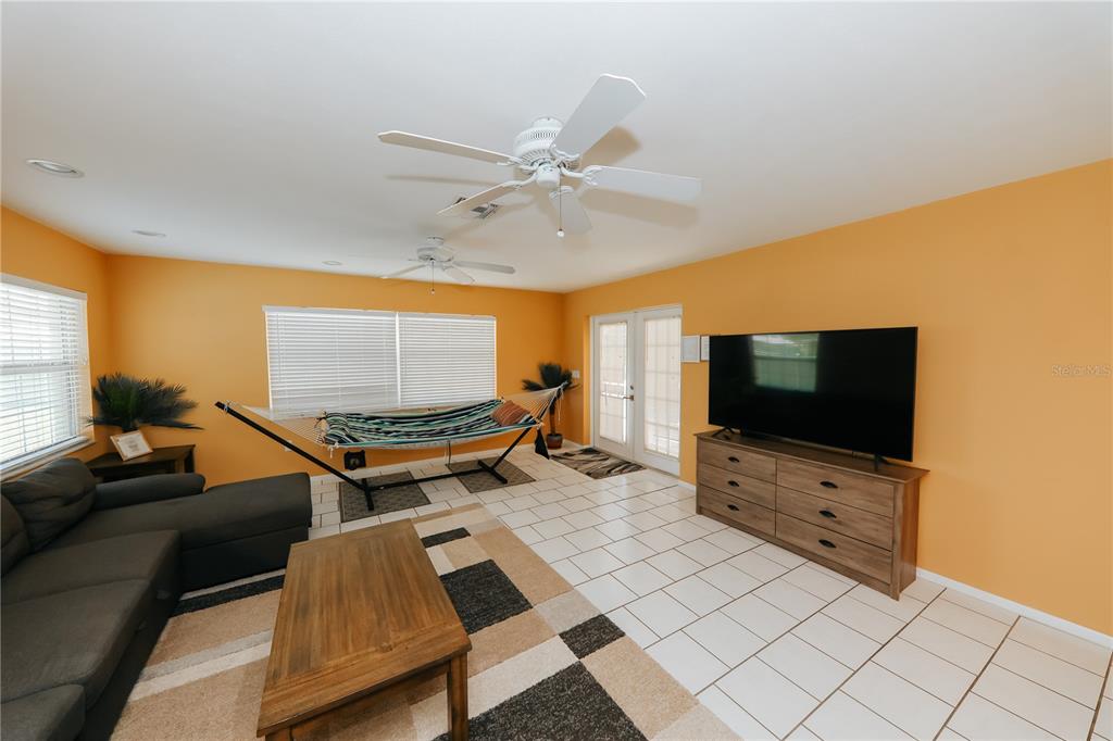 A living room features orange walls, white tile floors, a hammock, and a television console — 5211 24TH AVENUE DRIVE W, BRADENTON, FL