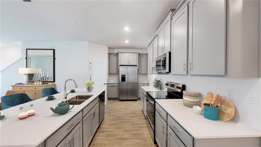 A modern kitchen features gray cabinets, stainless steel appliances, and a large white island — 5694 KETTLEBELL ALLEY, CLERMONT, FL