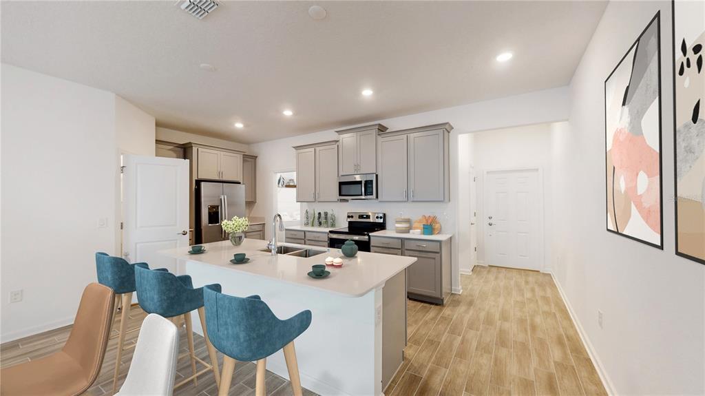 A kitchen features a central island with blue stools, grey cabinetry, and light wood flooring — 5694 KETTLEBELL ALLEY, CLERMONT, FL