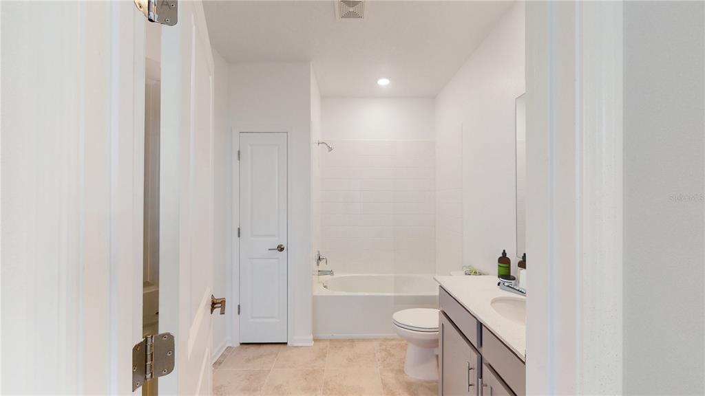 A bathroom features a white bathtub with a shower, a toilet, and a vanity cabinet — 5694 KETTLEBELL ALLEY, CLERMONT, FL