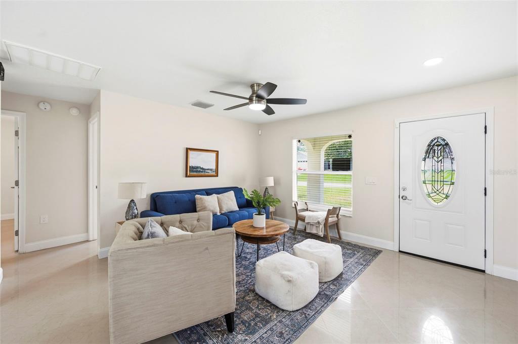 A living room features a blue sofa, a beige armchair, a round coffee table, and a rug — 5225 DEERFIELD AVENUE, SPRING HILL, FL