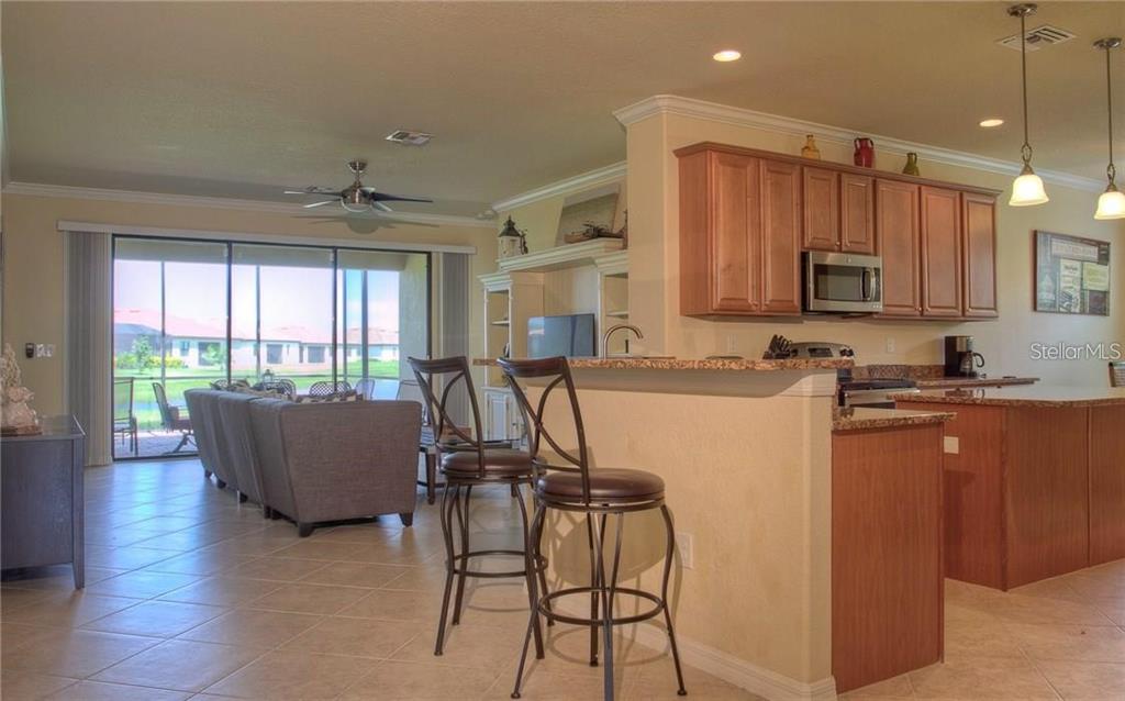 A kitchen with wood cabinets and a breakfast bar overlooks a living room with tile floors — 218 WHISPERING PALMS LANE, BRADENTON, FL